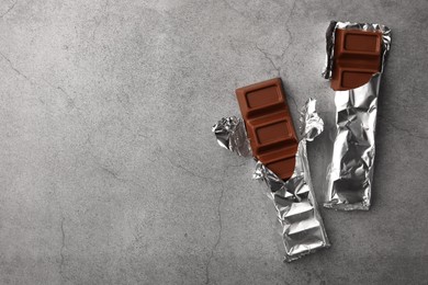 Photo of Tasty chocolate bars wrapped in foil on grey table, flat lay. Space for text