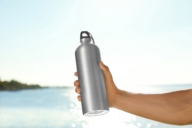 Young sporty man holding water bottle near river on sunny day