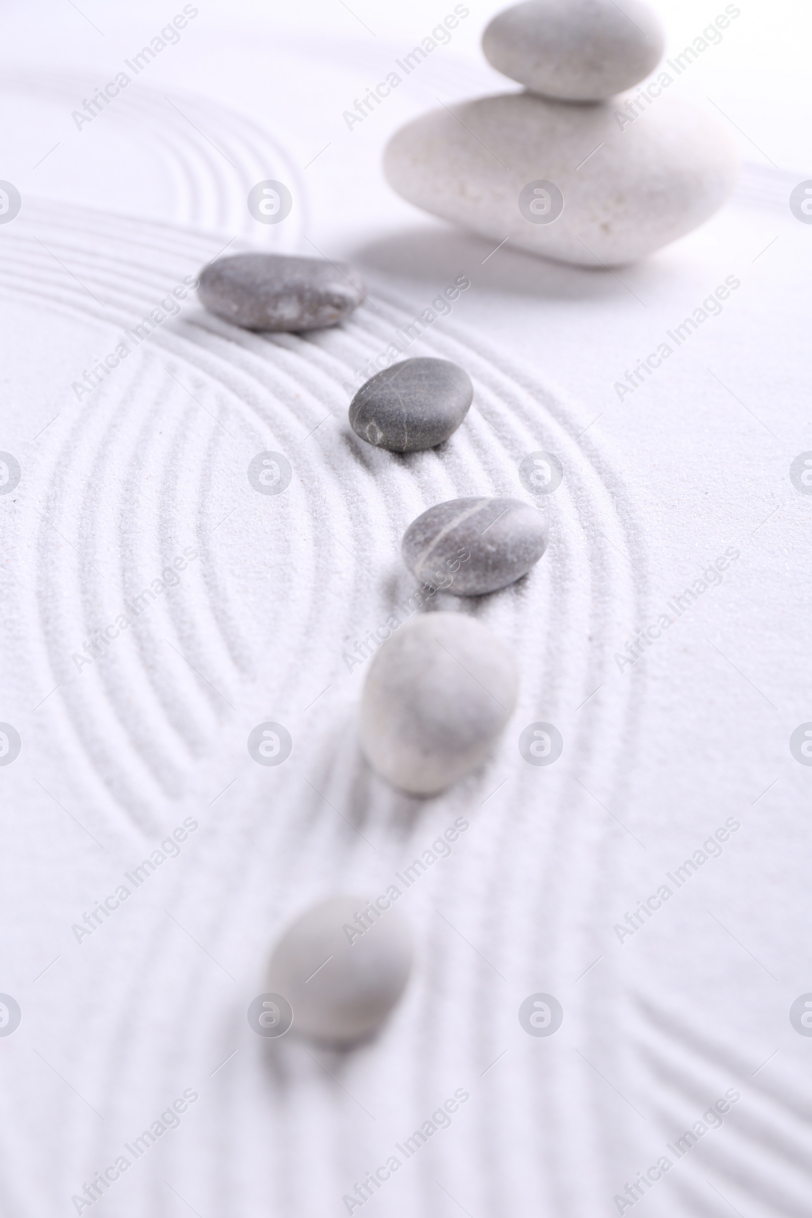 Photo of Zen garden stones on white sand with pattern, closeup