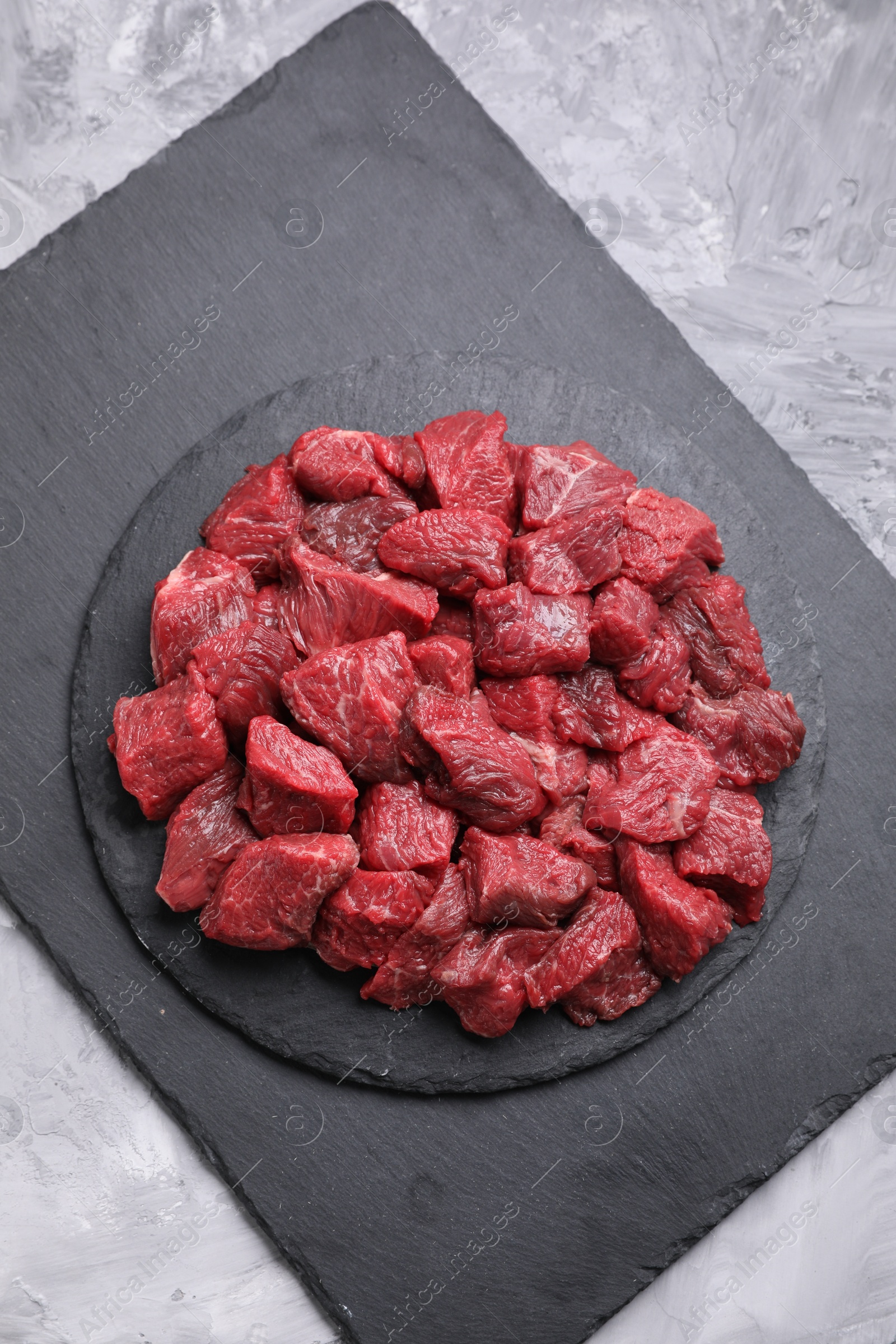 Photo of Pieces of raw beef meat on grey textured table, top view