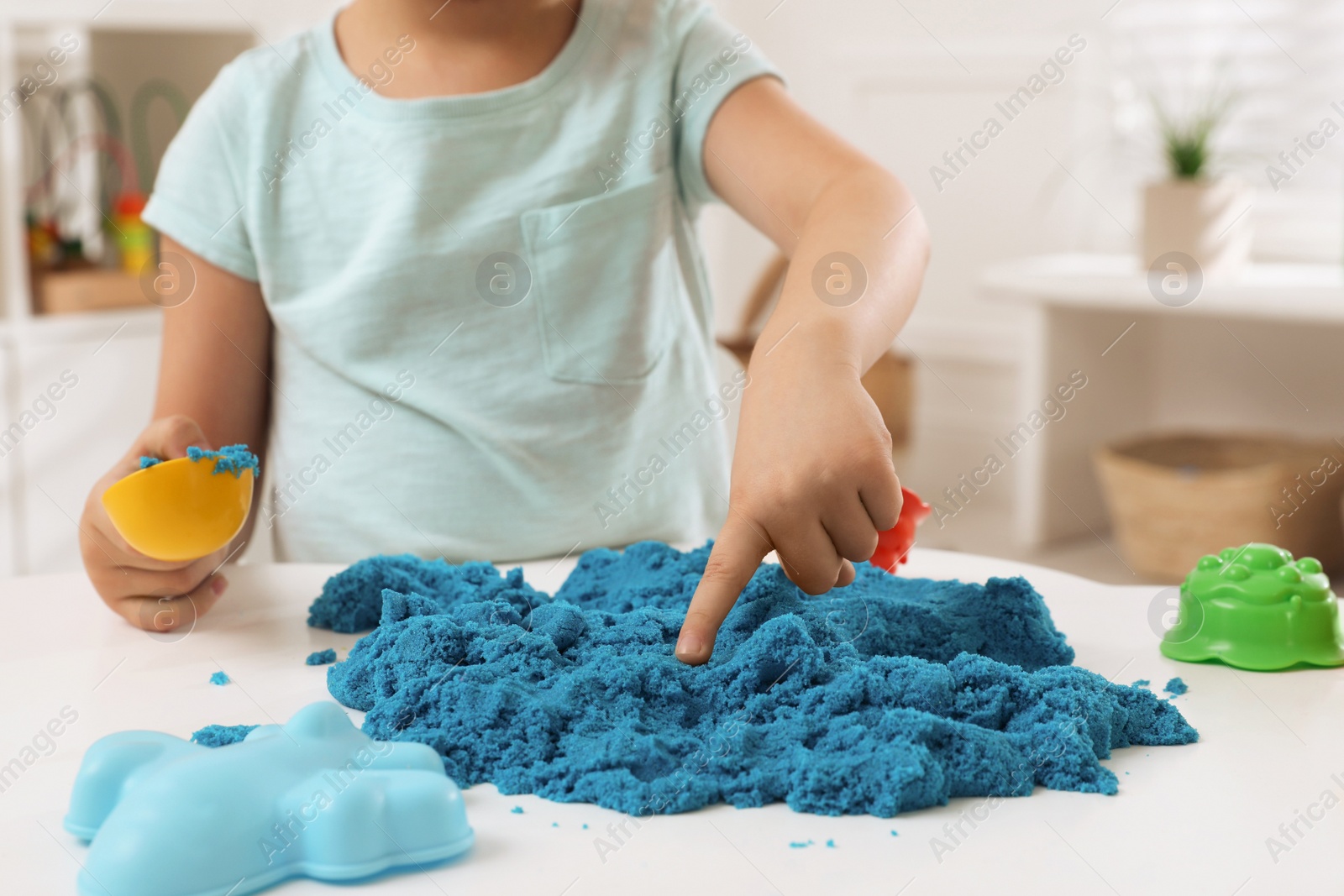 Photo of Little boy playing with bright kinetic sand at table indoors, closeup