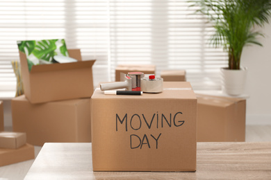 Photo of Cardboard box with words MOVING DAY and packaging items on wooden table