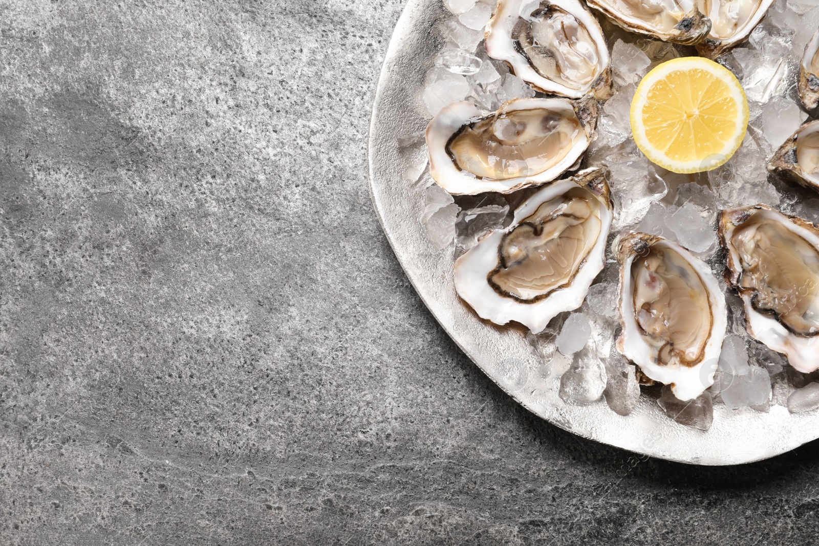 Photo of Delicious fresh oysters with lemon on grey table, top view. Space for text