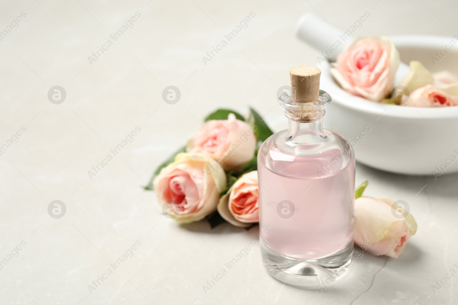 Photo of Bottle of rose essential oil and flowers on white table, space for text