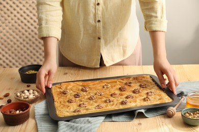 Photo of Woman with baking pan of delicious baklava at wooden table, closeup
