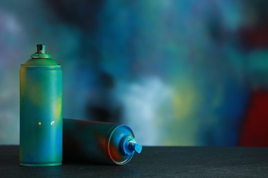 Two spray paint cans on gray surface against color background, space for text