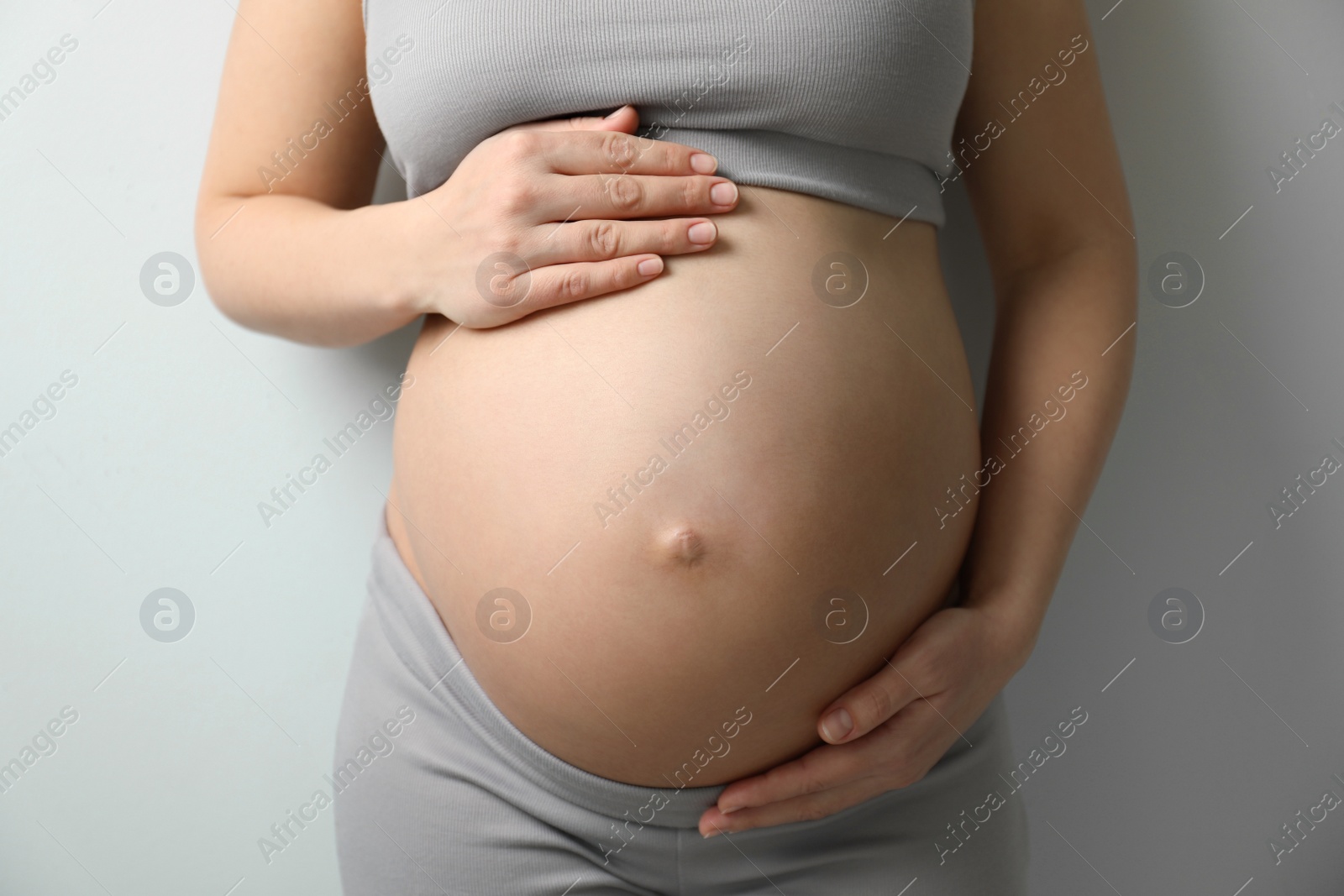 Photo of Pregnant young woman touching belly on light background, closeup