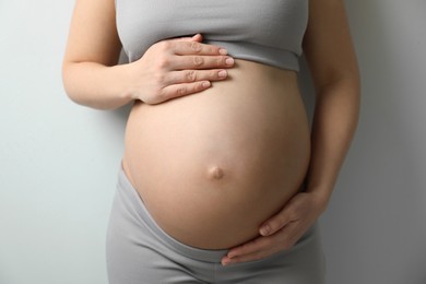 Pregnant young woman touching belly on light background, closeup