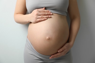 Photo of Pregnant young woman touching belly on light background, closeup