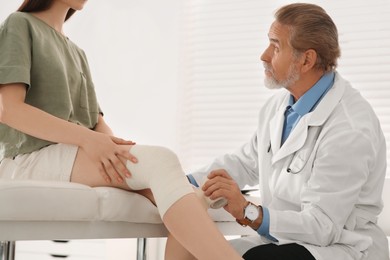 Orthopedist applying bandage onto patient's knee in clinic