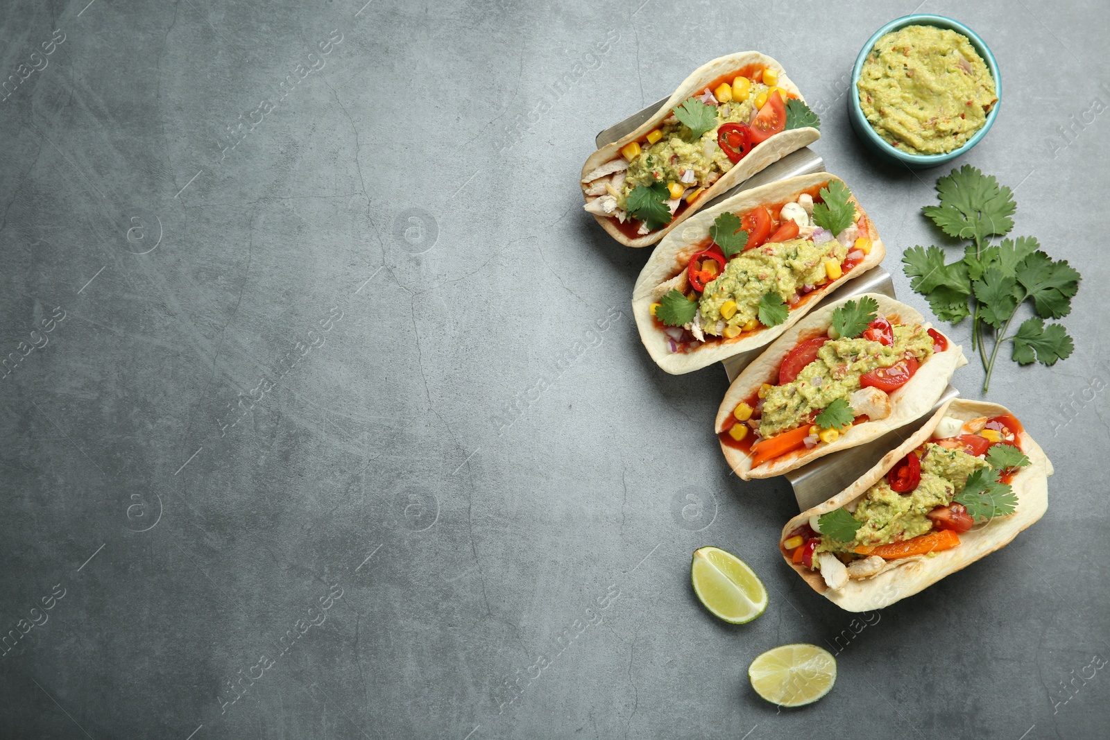 Photo of Delicious tacos with guacamole, meat and vegetables served on grey table, flat lay. Space for text