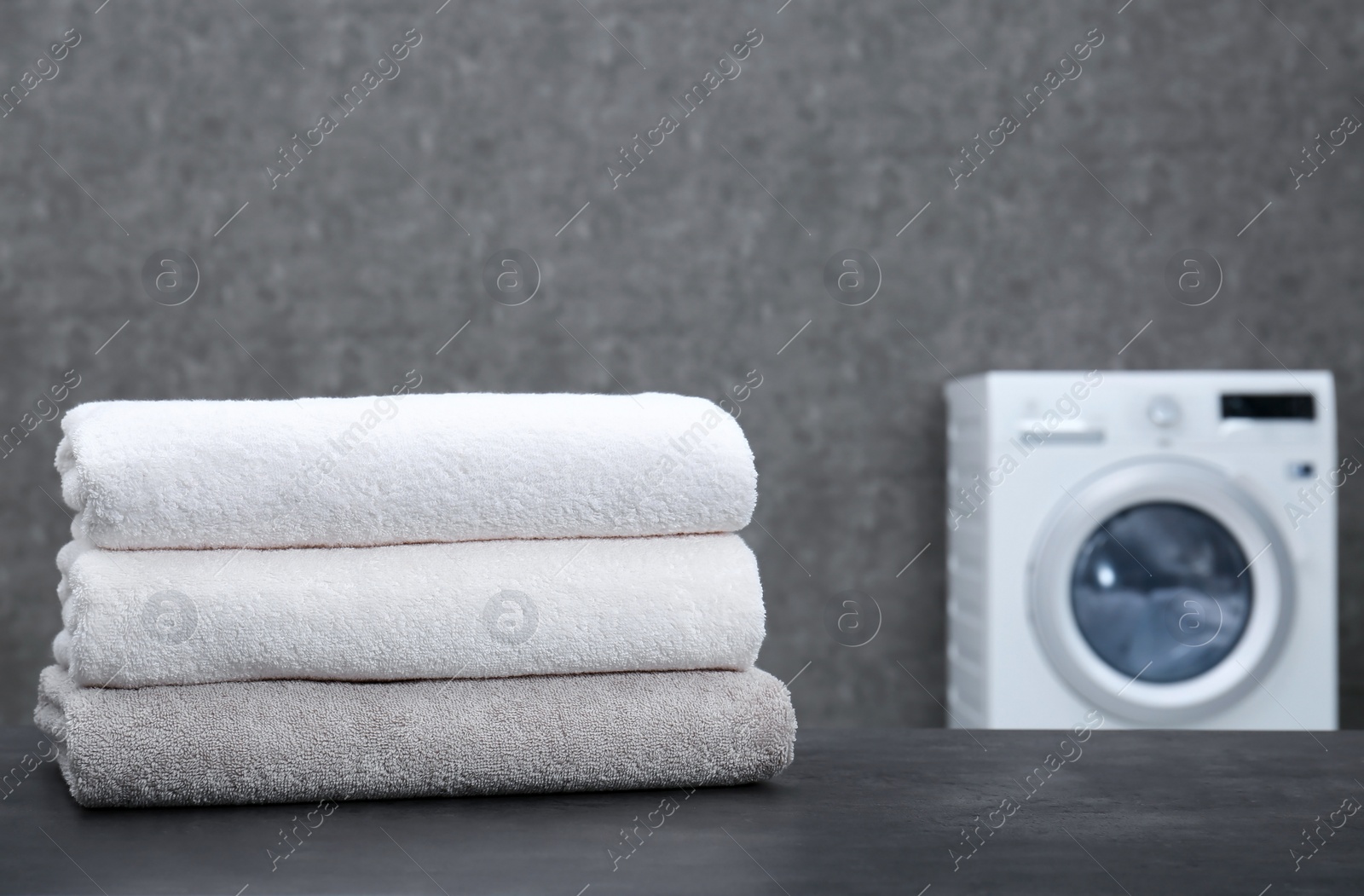 Photo of Stack of clean towels on table in laundry room. Space for text