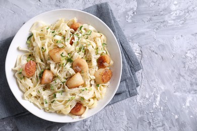 Delicious scallop pasta with spices in bowl on gray textured table, top view. Space for text