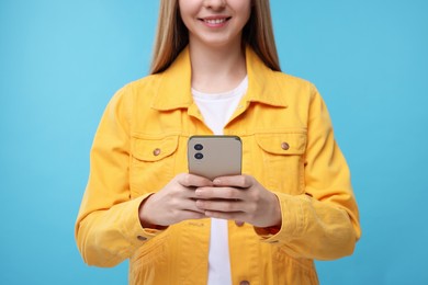 Woman sending message via smartphone on light blue background, closeup