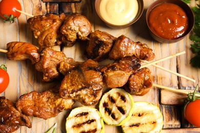 Photo of Delicious barbecued meat served with garnish and sauces on wooden background, top view