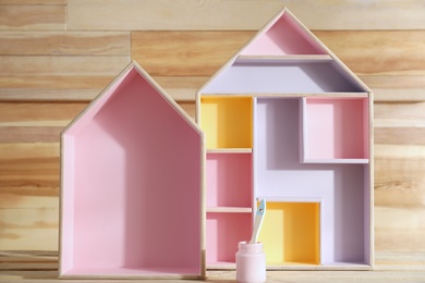 Photo of House shaped shelves and jar of pink paint with brush on wooden table. Interior elements