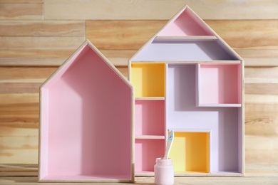 House shaped shelves and jar of pink paint with brush on wooden table. Interior elements