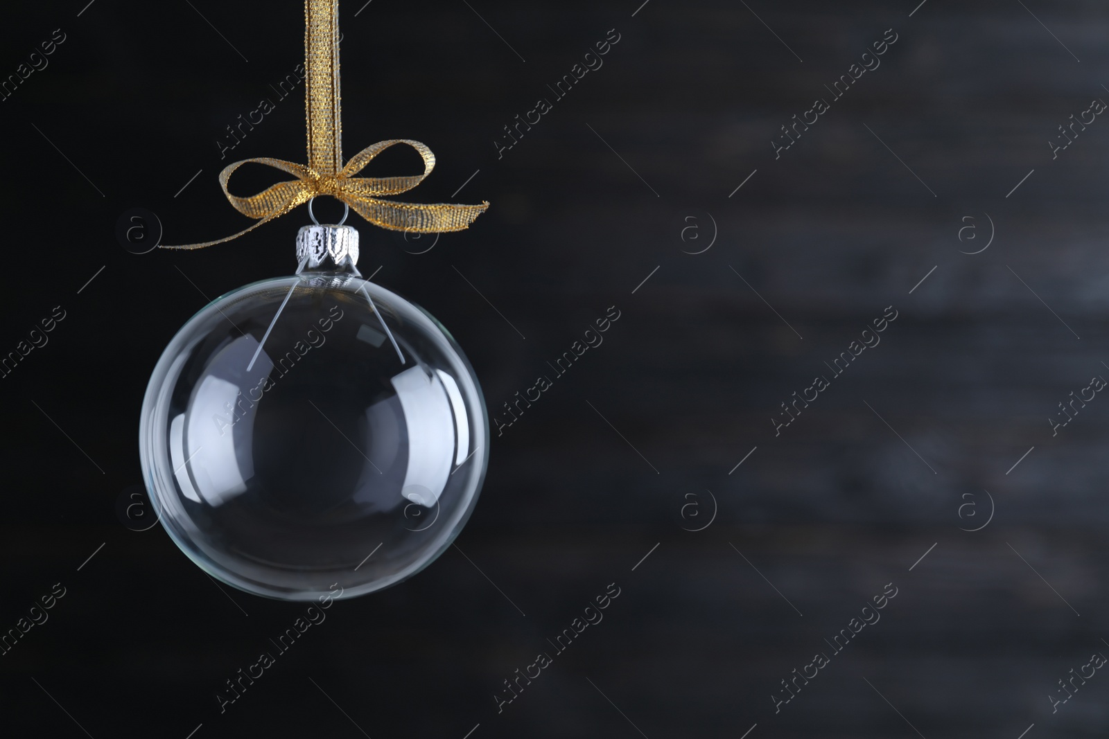 Photo of Transparent glass Christmas ball with golden ribbon and bow on dark background. Space for text