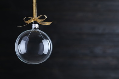 Photo of Transparent glass Christmas ball with golden ribbon and bow on dark background. Space for text