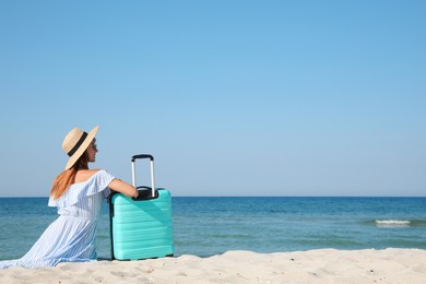 Photo of Woman with suitcase sitting on sandy beach near sea, back view