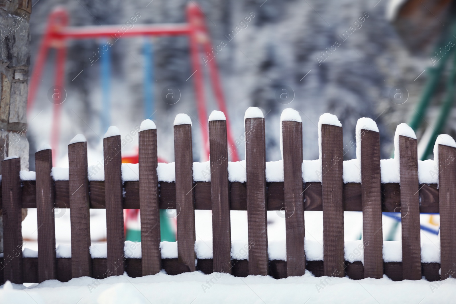 Photo of Wooden fence covered with snow near playground on winter day