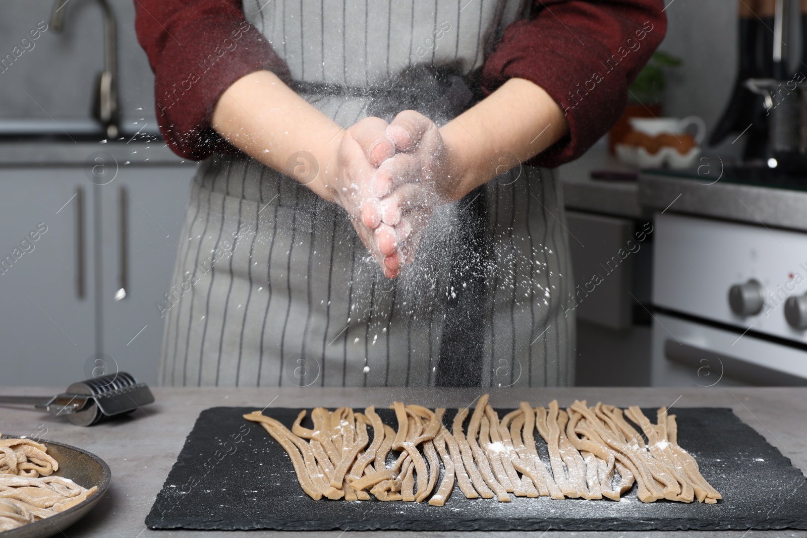 Photo of Woman sprinkling flour over uncooked soba at table in kitchen, closeup