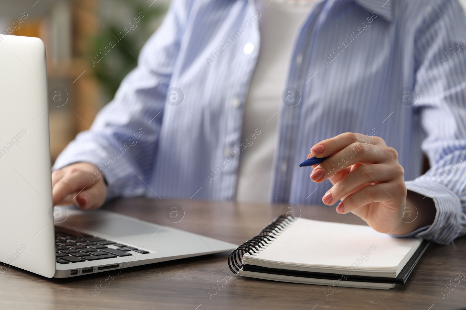 Photo of E-learning. Woman taking notes during online lesson at table indoors, closeup