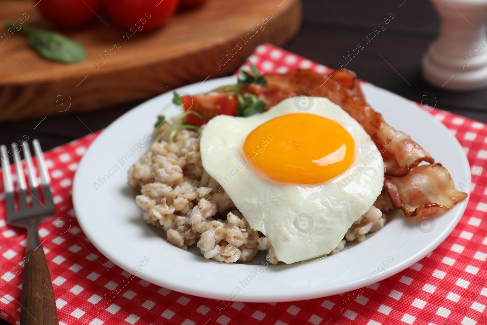 Photo of Tasty boiled oatmeal with fried egg, bacon and tomato served on table, closeup