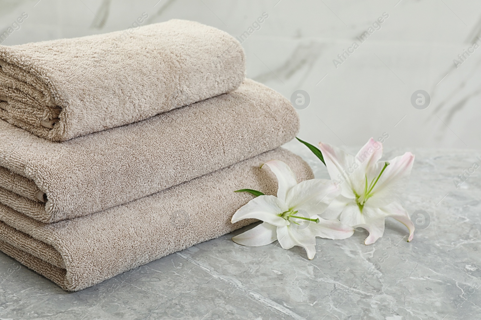 Photo of Stack of fresh towels with flowers on grey table against light background. Space for text