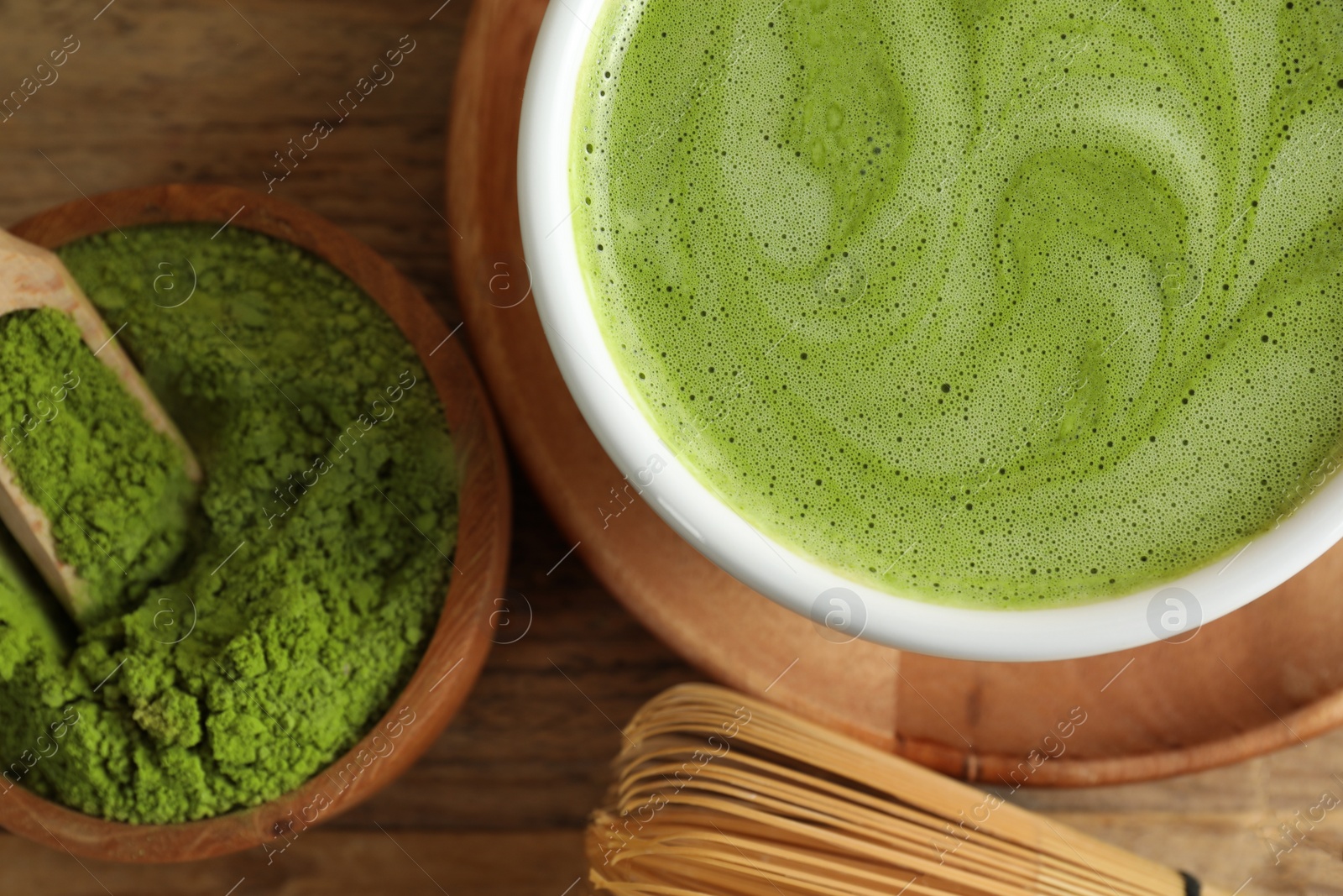 Photo of Cup of fresh matcha latte, powder and bamboo whisk on wooden table, flat lay