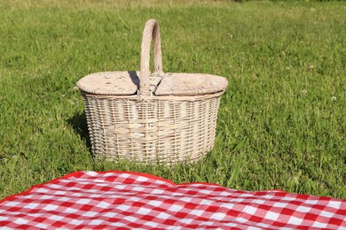 Photo of Picnic basket and checkered tablecloth on green grass outdoors