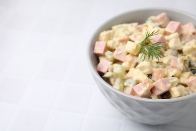 Photo of Tasty Olivier salad with boiled sausage in bowl on white tiled table, closeup. Space for text