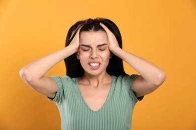 Photo of Woman suffering from migraine on yellow background