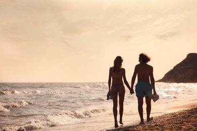 Photo of Young woman in bikini and her boyfriend walking on beach at sunset. Lovely couple