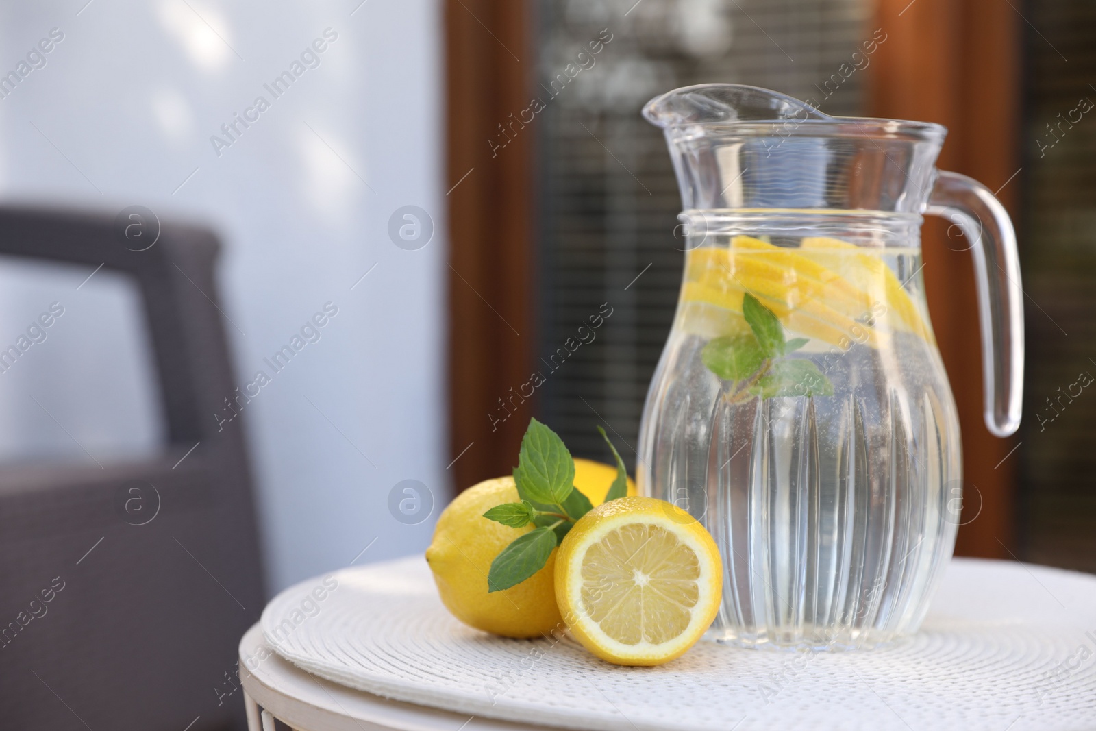 Photo of Jug of water with lemons and mint on white table outdoors