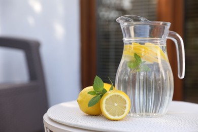 Jug of water with lemons and mint on white table outdoors