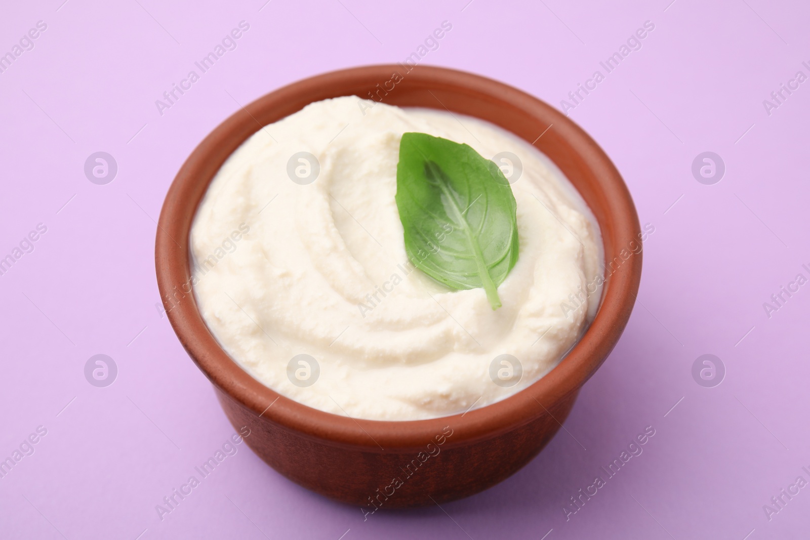 Photo of Delicious tofu sauce and basil leaf in bowl on violet background, closeup