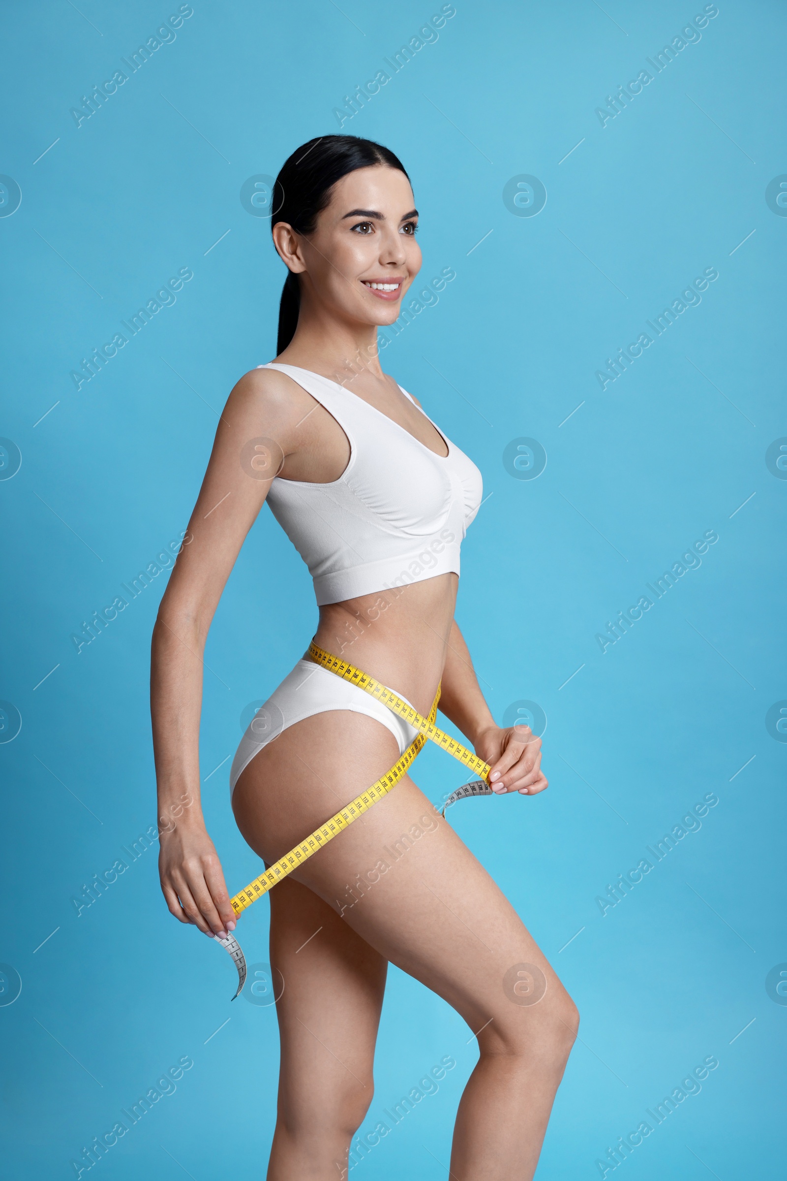Photo of Young woman measuring waist with tape on light blue background