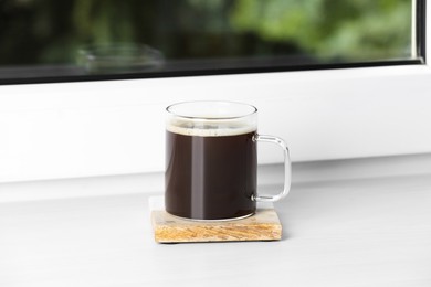Photo of Glass cup of coffee on wooden window sill
