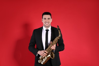 Young man in elegant suit with saxophone on red background