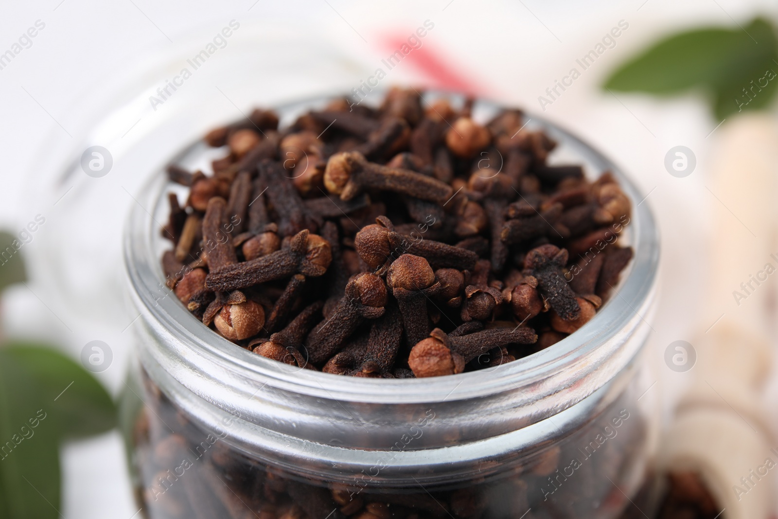 Photo of Aromatic cloves in glass jar on table, closeup