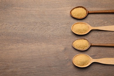 Photo of Spoons with brown sugar on wooden table, flat lay. Space for text