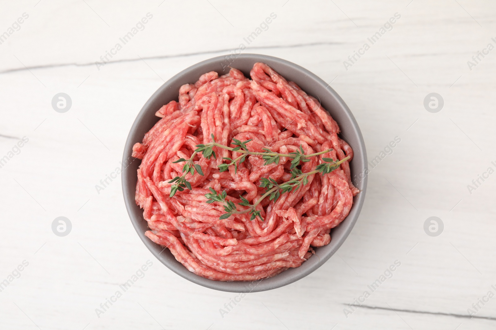 Photo of Fresh raw ground meat and thyme in bowl on white wooden table, top view