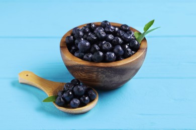 Photo of Ripe bilberries and leaves on light blue wooden table, closeup