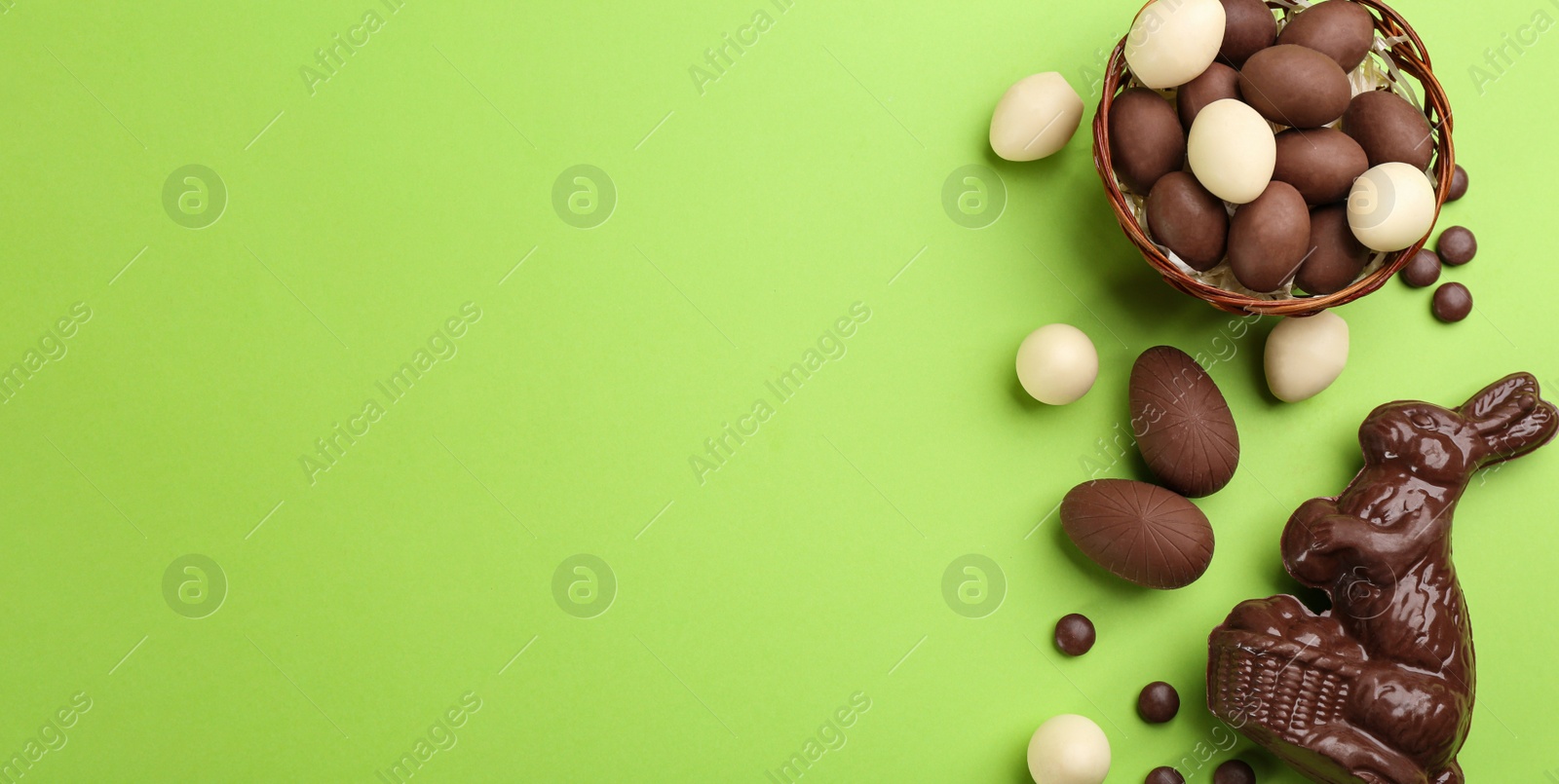 Photo of Flat lay composition with chocolate Easter bunny, eggs and candies on green background. Space for text