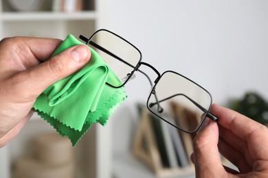 Man wiping glasses with microfiber cloth indoors, closeup