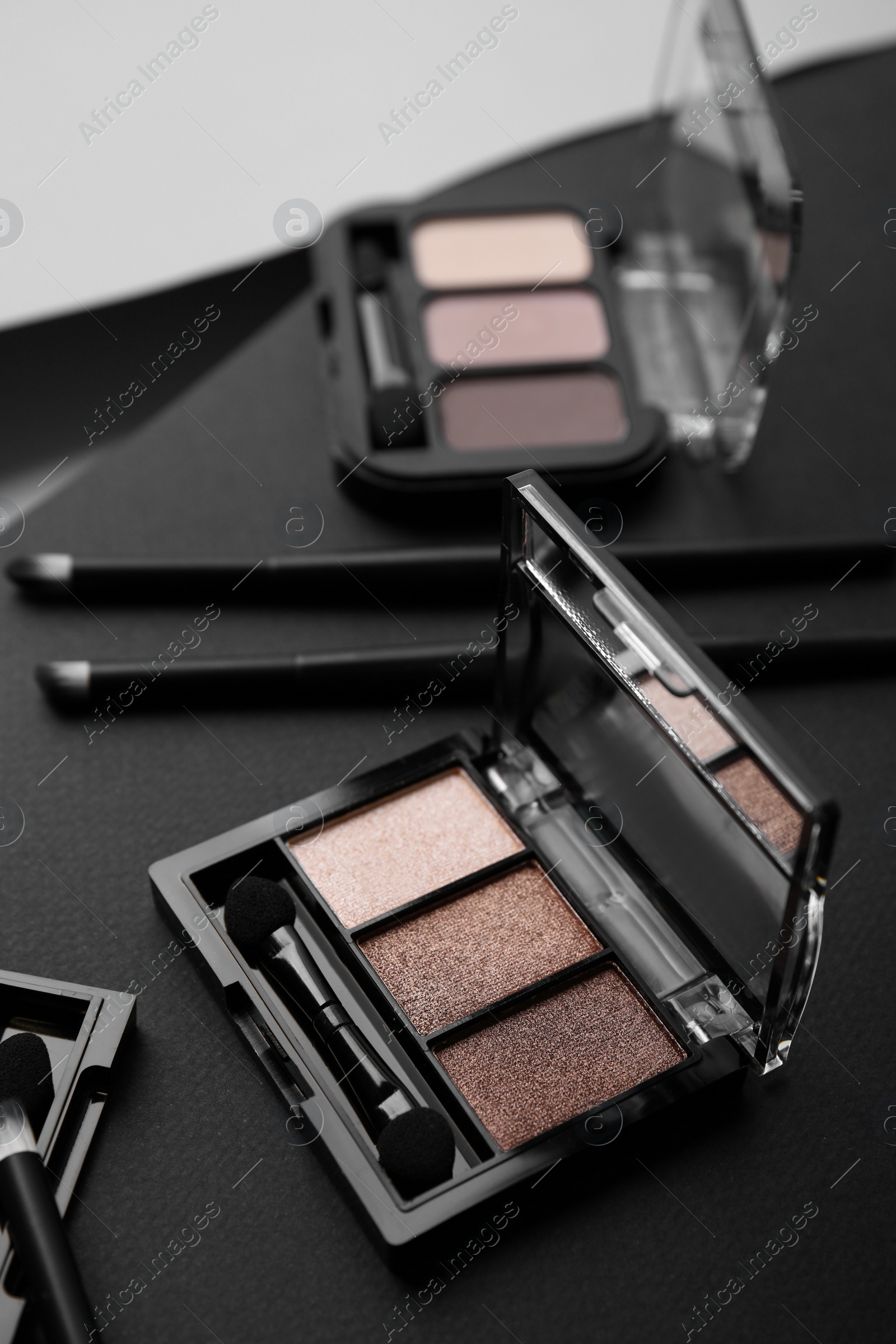 Photo of Eye shadow palettes and professional makeup brushes on black surface