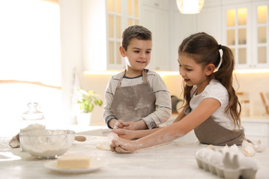 Cute little children cooking dough together in kitchen