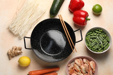 Black wok, chopsticks and products on color table, flat lay