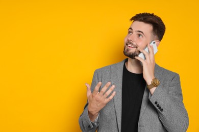 Photo of Handsome man in stylish grey jacket talking on phone against yellow background, space for text